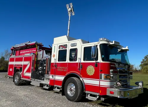 Pierce pumper front-right profile on gravel lot showing cab, pump panel area, and body compartments