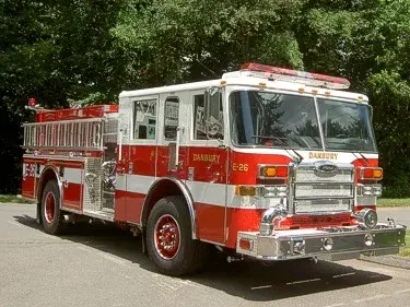 Front-left exterior view of a pumper showing enclosed cab, side pump panel section, and rear body.