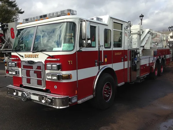 Front-left exterior view of tower ladder truck showing cab, ladder base, and tandem rear axles