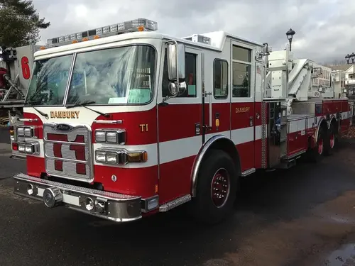 Front-left exterior view of tower ladder truck showing cab, ladder base, and tandem rear axles