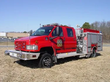 Front-left exterior view of a rescue pumper with commercial cab, side pump panel, and rear body compartments.
