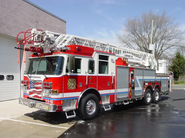Front-left exterior view of a ladder truck with stowed aerial, side compartments, and tandem rear axles.