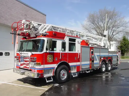 Front-left exterior view of a ladder truck with stowed aerial, side compartments, and tandem rear axles.