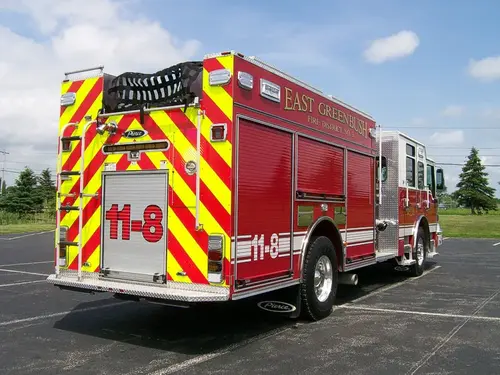 Rear-left exterior view showing red-yellow chevrons, rear ladder, hosebed netting, and side roll-up doors.