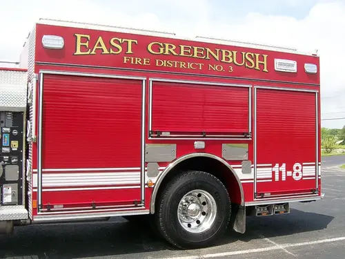 Driver-side body close-up showing roll-up compartment doors, rear wheel area, and EAST GREENBUSH FIRE DISTRICT NO. 3 lettering.