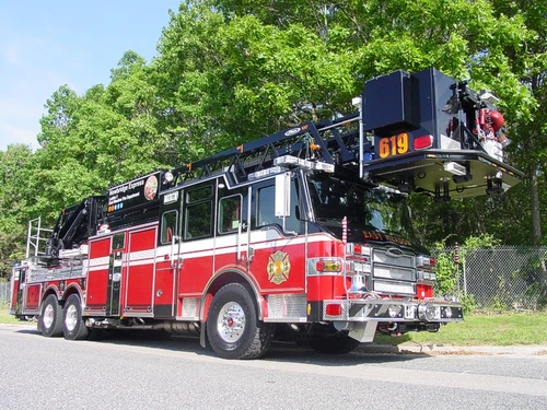 Front-right exterior view of a tower ladder with stowed bucket, side compartments, and tandem rear axles.