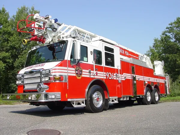 Front-right exterior view of a rear-mount aerial ladder with front outrigger, side compartments, and tandem rear axles.