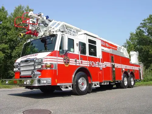 Front-right exterior view of a rear-mount aerial ladder with front outrigger, side compartments, and tandem rear axles.