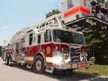 Aerial ladder truck front-left exterior view showing enclosed cab and ladder sections