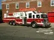 Aerial ladder truck side view near station showing ladder bed and tandem axles