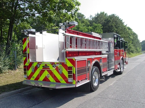 Rear-left exterior view showing rear chevrons, side ladder storage, and rear body compartments.