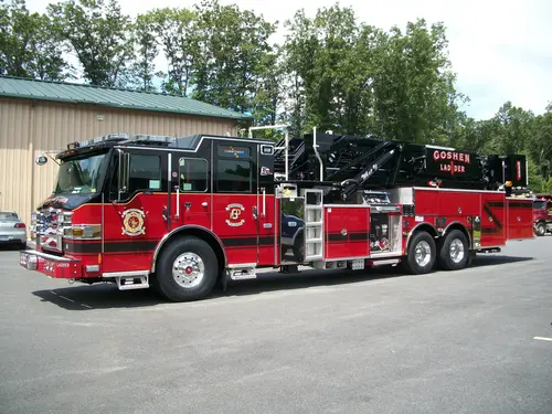 Driver-side full profile of a ladder truck with stowed aerial, side compartments, and tandem rear axles.
