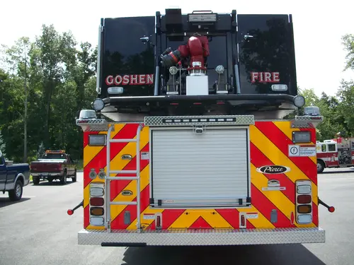 Straight rear view with red-yellow chevrons, rear ladder, aerial nozzle assembly, and center rear roll-up door.