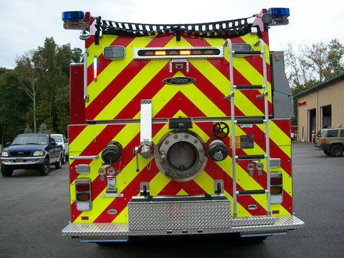 Straight rear view with red-yellow chevrons, rear intake connections, tail lights, and access ladder.