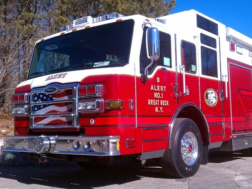 Front-left close view of a pumper showing the cab, grille, bumper, and driver-side body compartments.
