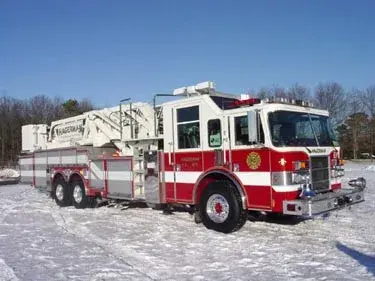 Front-left exterior view of tower ladder truck on snow showing stowed aerial and tandem rear axles