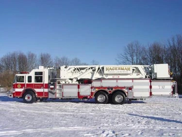Driver-side full profile showing tower ladder body, side compartments, and tandem wheels