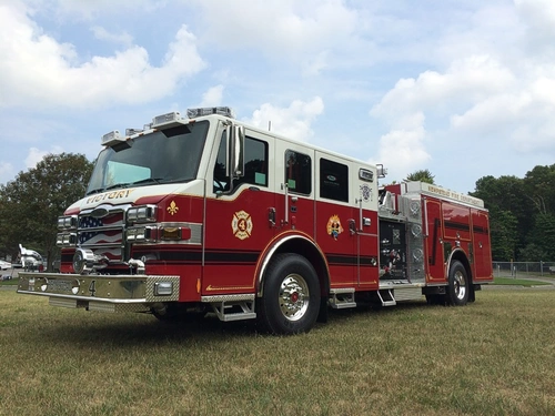 Front-left exterior view of a pumper showing the cab, bumper, pump panel area, and side compartments.