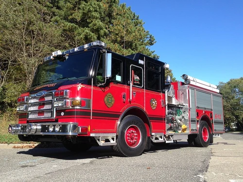 Front-left exterior view of a pumper showing the cab, bumper, pump panel section, and side compartments.