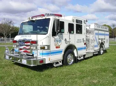 Front-left exterior view of a pumper showing enclosed cab, side pump panel area, and rear body compartments.