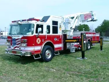 Front-left exterior view of tower ladder truck with outriggers deployed on grass