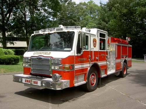 Front left exterior view of the pumper with chrome bumper, cab roof lights, and side body compartments.