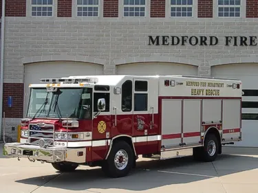Front left exterior view of the heavy rescue with chrome bumper, cab lights, and side roll-up compartments.