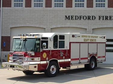 Front left exterior view of the heavy rescue with chrome bumper, cab lights, and side roll-up compartments.