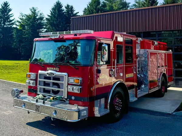 Front left exterior view of the pumper with chrome bumper, grille, pump panel side, and hosebed area visible.