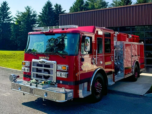 Front left exterior view of the pumper with chrome bumper, grille, pump panel side, and hosebed area visible.