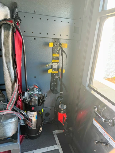 Rear cab corner interior showing firefighter seat, mounted extinguisher, wall brackets, and doorway access.