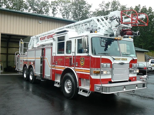 Front-right exterior view of a ladder truck with stowed aerial, side compartments, and tandem rear axles.