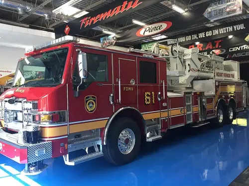 Front left exterior view of the tiller aerial with chrome bumper, cab, tandem rear axles, and stowed ladder visible.