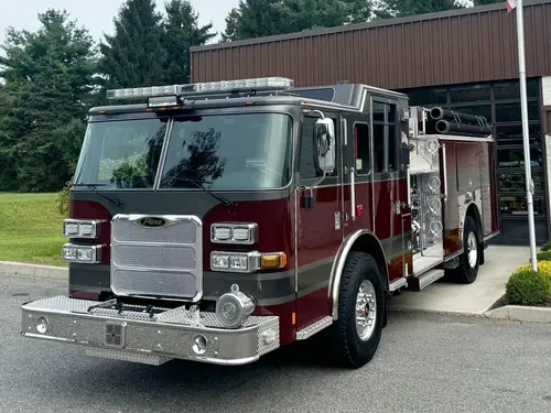 Front-right exterior view of a pumper showing the grille, bumper, cab, and side pump panel section.