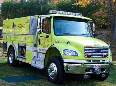 Front right angle showing cab doors, bumper, and side compartment body with top edge warning lights.