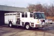 Wide front right view of the parked pumper with bumper, cab, and side compartments visible.