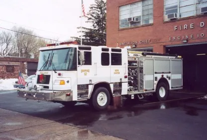Front right exterior view of a white pumper with chrome bumper, side pump controls, and roll-up compartments.