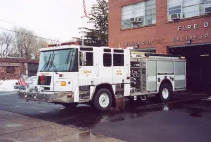 Front right exterior view of a white pumper with chrome bumper, side pump controls, and roll-up compartments.