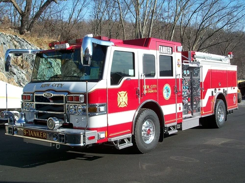 Front-left exterior view of a tanker pumper showing the cab, bumper, pump panel, and side compartments.