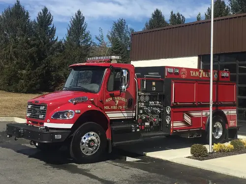 Front left exterior view of a tanker with commercial cab, black front bumper, midship pump panel, and side compartments.