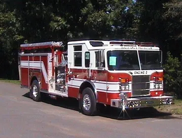 Front-left exterior view of a pumper showing the enclosed cab, side pump panel area, and rear body compartments.