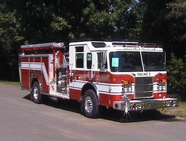 Front-left exterior view of a pumper showing the enclosed cab, side pump panel area, and rear body compartments.