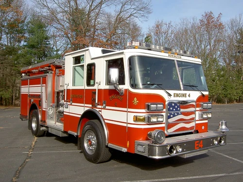 Front right exterior view of the pumper with chrome bumper, flag-style grille, and side body compartments.