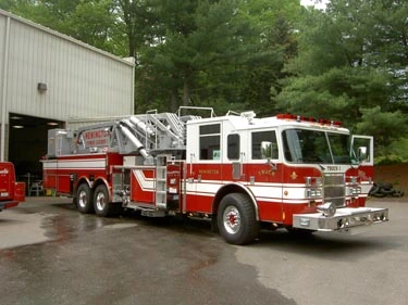 Front right exterior view of a mid-mount tower ladder with tandem rear axles and stowed aerial section.
