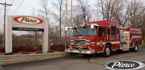 Front-left exterior view of a pumper parked beside a Pierce sign showing cab and side body profile.