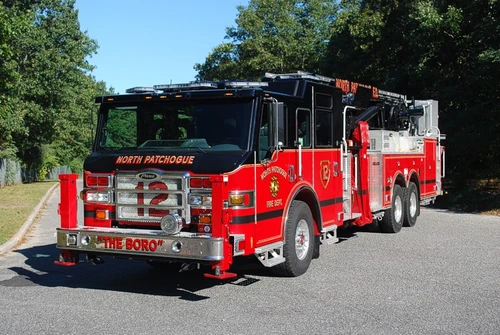 Front-left exterior view of a tower ladder with front outrigger deployed, side compartments, and tandem rear axles.