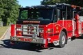 Wide front-left view of the tower ladder parked on the roadway with front outrigger visible.