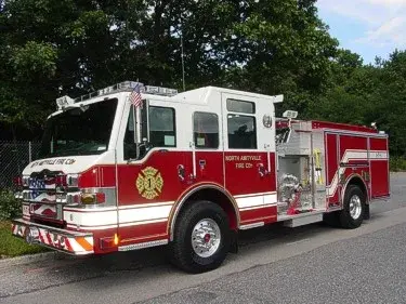 Front-left exterior view of a pumper showing the cab, bumper, pump panel area, and side compartments.