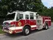 Wide front-left view of the pumper parked roadside with cab and side body profile visible.