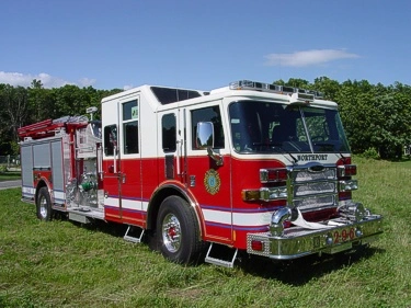 Front left exterior view of the pumper with chrome bumper, cab roof lights, and side pump panel area visible.